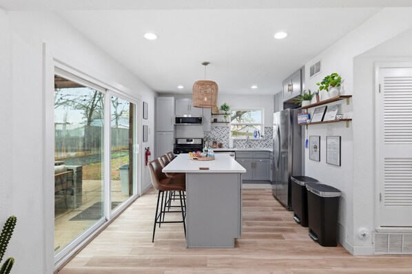 A modern kitchen with a central island, white cabinetry, and a large window. - Cozy Walk to AT&T Stadium! Game Day Retreat!Family Friendl (Arlington)