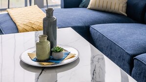 A modern living room with a blue sofa, a marble coffee table, and a view of the city through large windows.