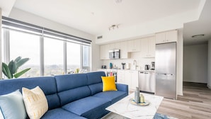 A modern living room with a blue sofa, a coffee table, and a view of the city through large windows.