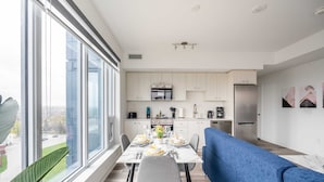 A modern kitchen with white cabinets, a stainless steel refrigerator, and a dining area with a blue sofa and a table set for two.