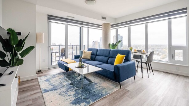 A modern living room with a blue sofa, a glass coffee table, and a city view through large windows.