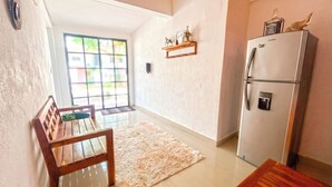 Una cocina con refrigerador, una silla de madera, un tapete y una ventana con vista a follaje.