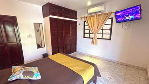 Un dormitorio con cama, televisor, armario, espejo y ventana con cortinas.