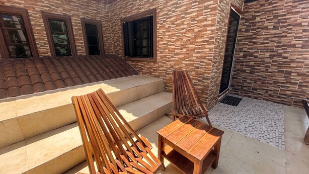 Un espacio exterior moderno con un muro de piedra, un banco de madera, una mesa y un juego de escalones que conducen a un techo cubierto.