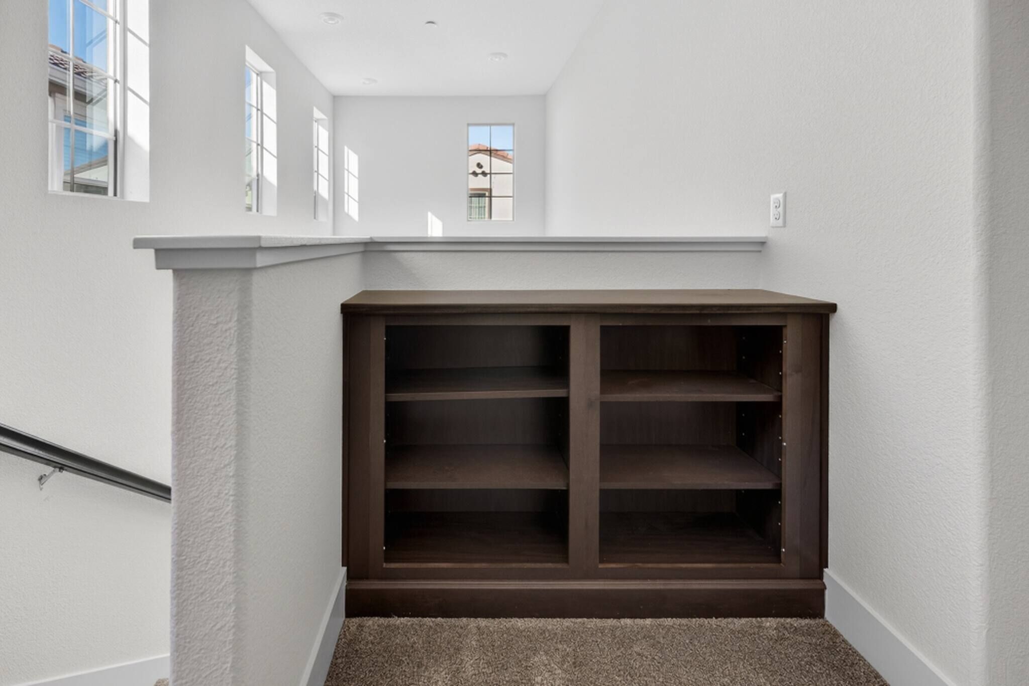 Une pièce d’angle dotée d’une bibliothèque intégrée en bois, d’un sol recouvert de moquette et d’un mur blanc avec une fenêtre.