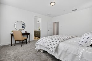Ein Schlafzimmer mit Bett, Stuhl, Schreibtisch, Spiegel und Tür.