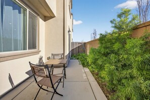 Eine Terrasse mit Tisch und Stühlen, ein Holzzaun und ein Heckenstreifen.