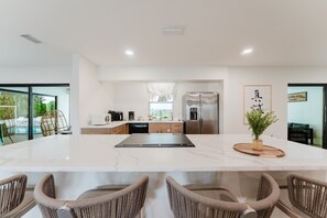 A modern kitchen with a large island, built-in appliances, and a view of a pool. - Deluxe Waterfront Villa | BBQ, Pool and Game Room (West Palm Beach)