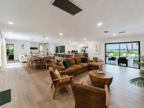 A spacious living area with a large window, a dining area, and a kitchen. - Deluxe Waterfront Villa | BBQ, Pool and Game Room (West Palm Beach)
