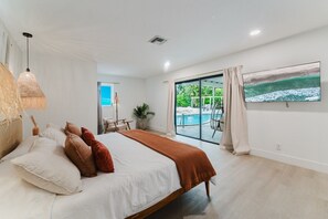 A bedroom with a bed, bedside table, lamp, and a view of an outdoor swimming pool. - Deluxe Waterfront Villa | BBQ, Pool and Game Room (West Palm Beach)