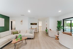 A spacious living room with a sofa, coffee table, and a view of the outdoor pool area. - Deluxe Waterfront Villa | BBQ, Pool and Game Room (West Palm Beach)