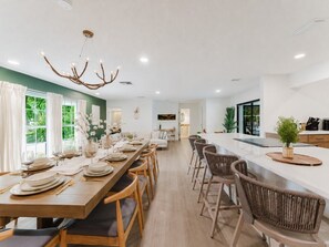 A modern dining area with a long wooden table set for a meal, surrounded by wicker chairs. - Deluxe Waterfront Villa | BBQ, Pool and Game Room (West Palm Beach)
