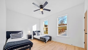 Ein Schlafzimmer mit zwei Betten, einem Deckenventilator und großen Fenstern.