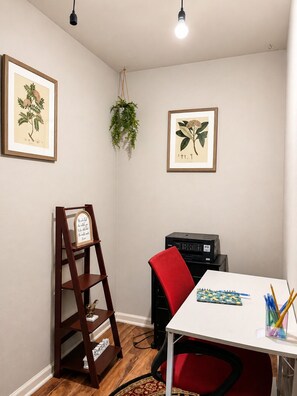 Ein Zimmer mit Schreibtisch, Stuhl, Drucker, gerahmten botanischen Zeichnungen und einer Holzleiter.
