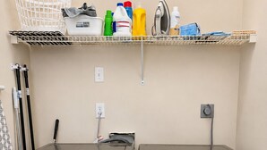 Dos lavadoras Samsung de carga frontal en un cuarto de lavado, con un estante superior que contiene productos de limpieza y una cesta.