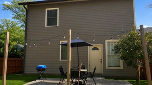 Una casa de dos pisos con un patio, una parrilla y luces colgantes.