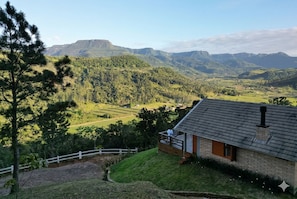 A house with a brick exterior, a wooden deck, and a view of rolling hills and mountains.