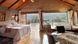 A spacious room with a high ceiling, a large bed, a dining table, and a view of the outdoors. - Chalet 2 - Mountain Range: Design with Hot Tub in the Canyons - Comfort 7km from the Center (Praia Grande)
