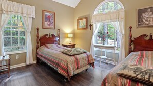 Quarto com uma cama grande, uma cama menor, uma mesinha de cabeceira, um abajur e uma janela com cortinas.