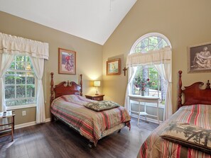 A bedroom with a large bed, a smaller bed, a nightstand, a lamp, and a window with curtains.