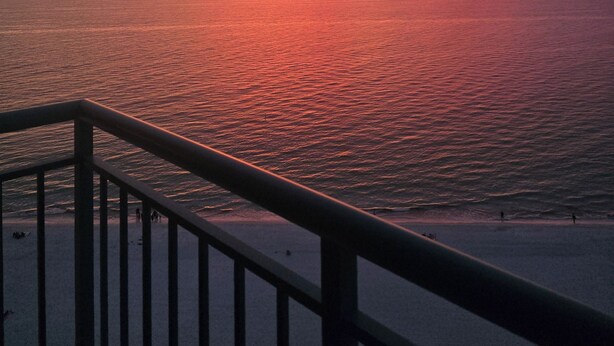 Um pôr do sol sobre o oceano, com um corrimão em primeiro plano.