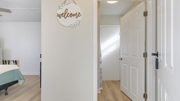Une chambre à coucher comprenant un lit, une table de chevet, un panneau d’accueil fixé au mur, et un couloir menant à une porte.