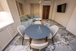 A modern living room with a sofa, a dining table with chairs, a TV mounted on the wall, and a door. - Private Villa - Poolside Retreat | Sea View & Calm Escape (Stelida)