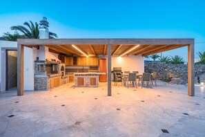 An outdoor kitchen area with a stone countertop, wooden cabinets, and a grill. - Private Villa - Poolside Retreat | Sea View & Calm Escape (Stelida)