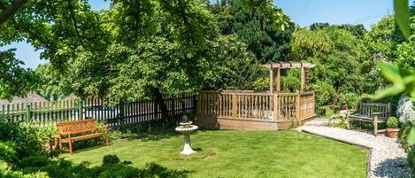 A well-maintained garden with a wooden pergola, a fountain, and a bench.