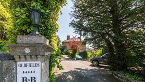 Un panneau de signalisation indiquant l’emplacement du « Oldfields B&B », entouré de verdure et de voitures garées.