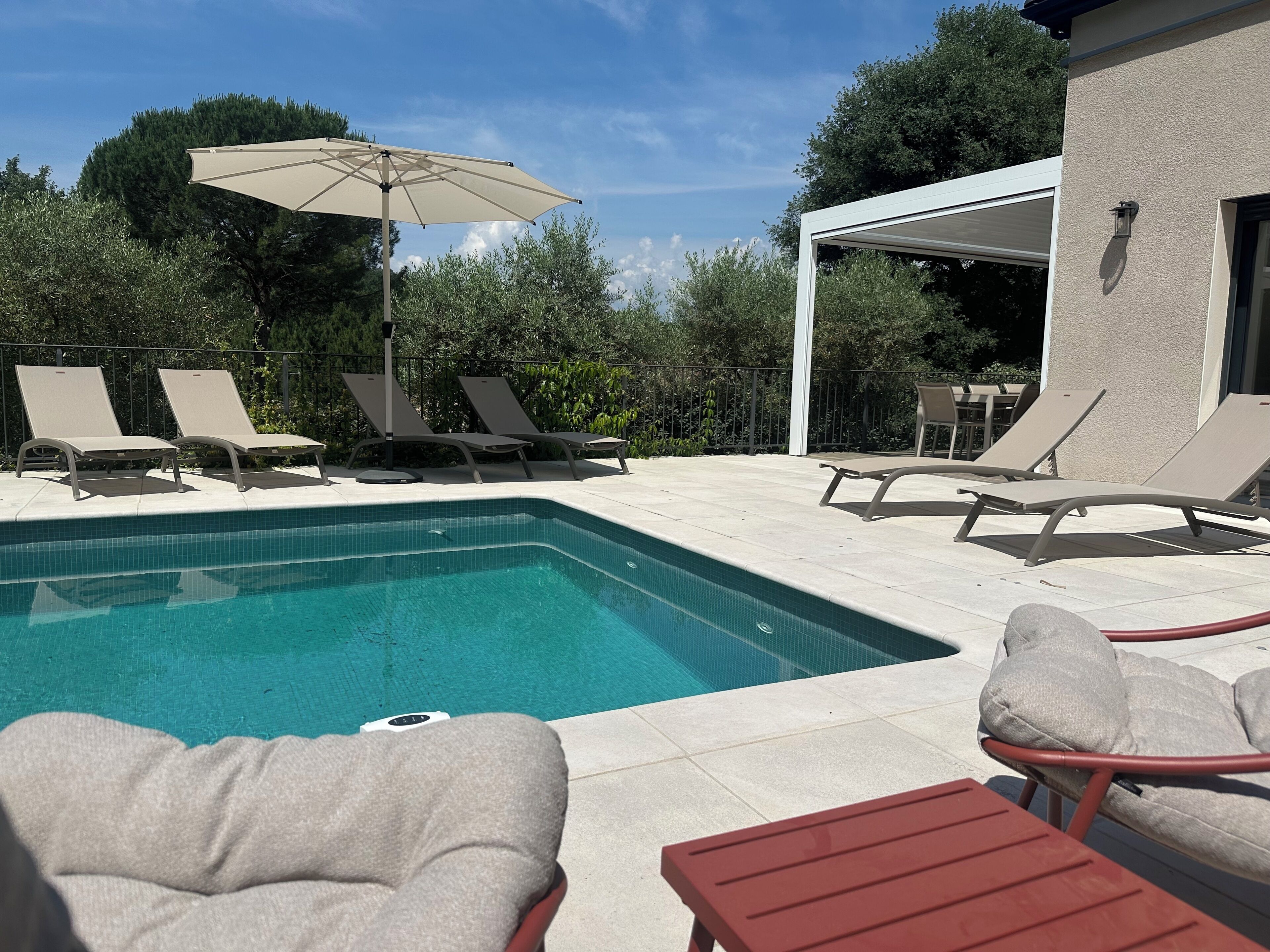 A swimming pool with lounge chairs and a table, surrounded by a fence and trees.