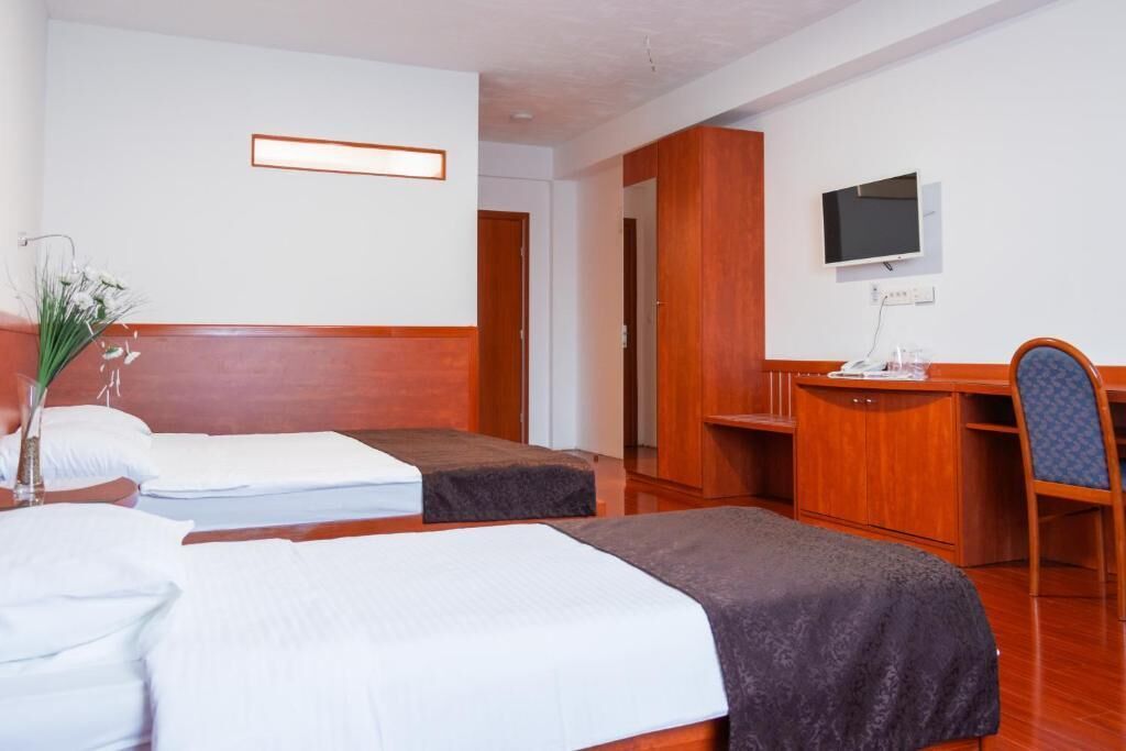 Een hotelkamer met twee eenpersoonsbedden, een bureau met stoel, een televisie en een kleine tafel.