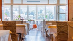 A restaurant with a long table layout, large windows, and potted plants.