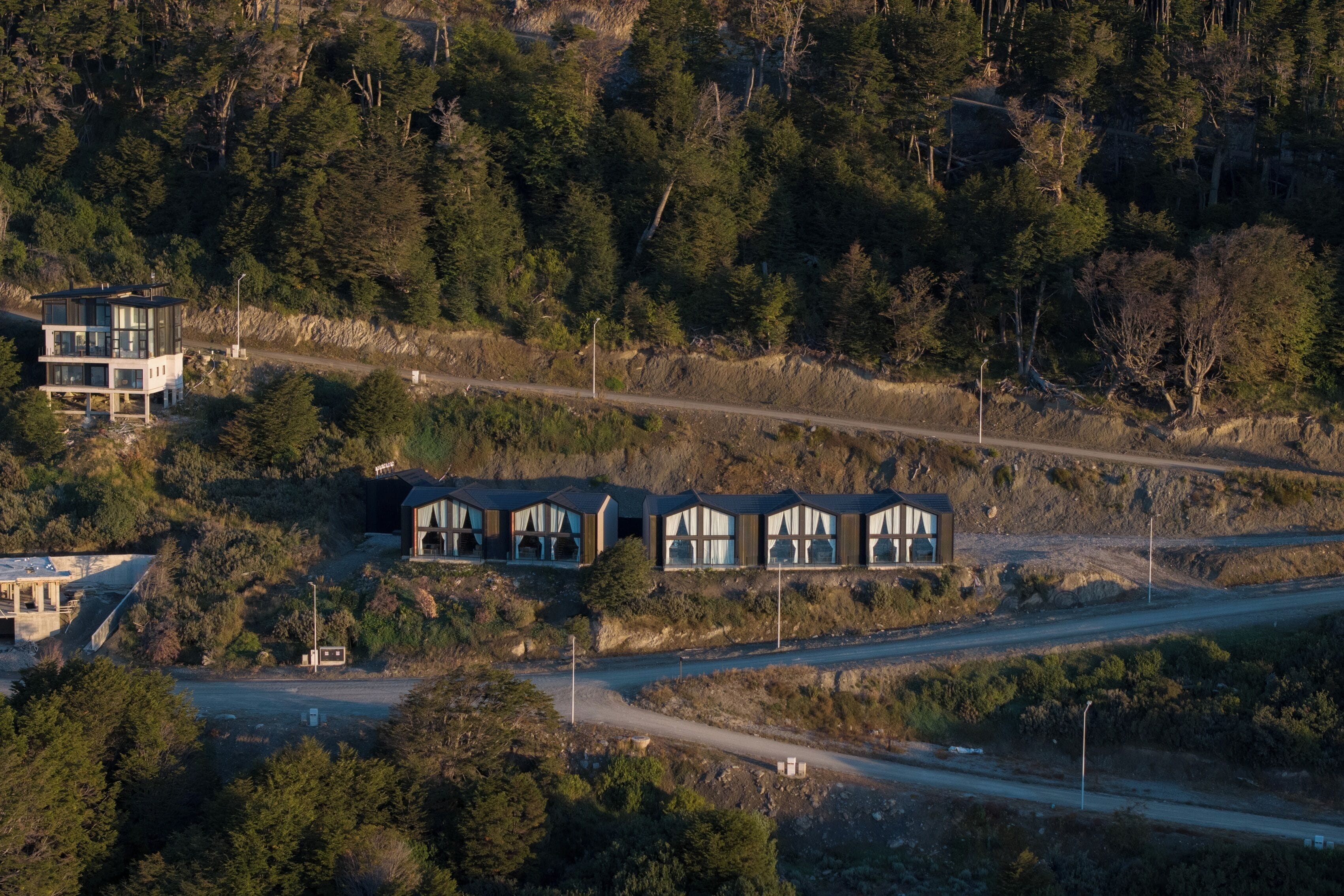 A cluster of modern cabins with large windows, surrounded by dense forest and a dirt road.