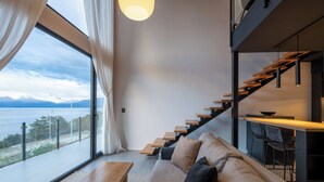 A modern interior with a sofa, wooden staircase, and a view of the sea.