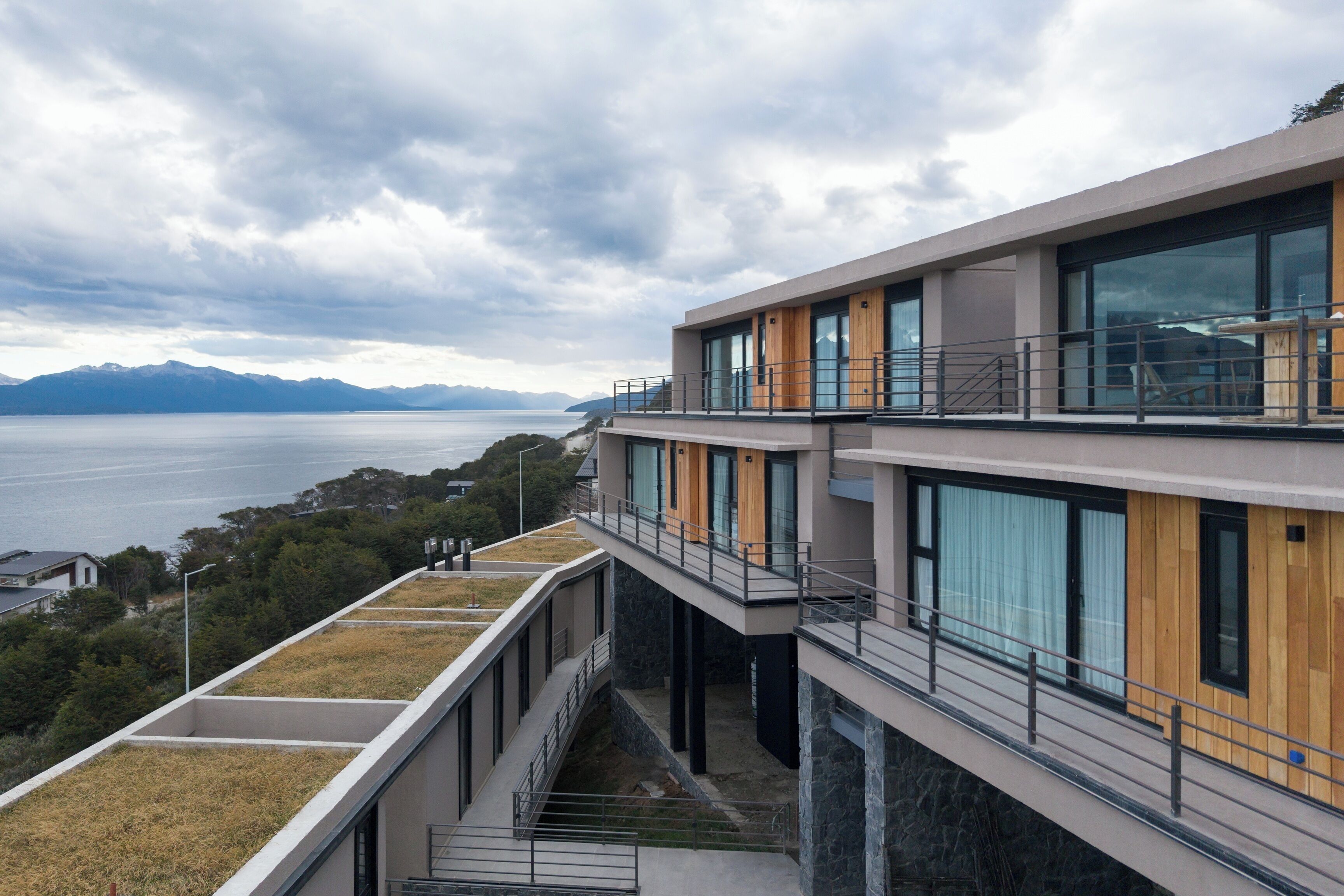 A modern building with a flat roof, large windows, and a view of a body of water and mountains.