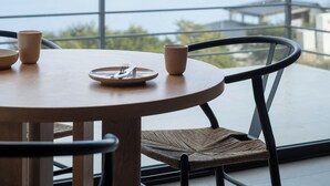 A round wooden table with chairs, a hanging light fixture, and a view of a body of water with mountains in the background.
