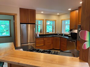 A modern kitchen with wooden cabinets, a stainless steel refrigerator, a gas stove, and a microwave. - Spacious Family Retreat Near Cowichan Bay. Sleeps 8. Yard, BBQ, Quiet & Private (Cowichan Bay)