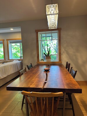A dining area with a large wooden table, chairs, a hanging light fixture, and a window with a view of greenery. - Spacious Family Retreat Near Cowichan Bay. Sleeps 8. Yard, BBQ, Quiet & Private (Cowichan Bay)