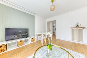 Moderni olohuone, jossa on litteänäyttöinen televisio, valkoiset huonekalut, puulattia ja patteri.