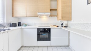 Une cuisine moderne avec des meubles blancs, un four noir et un plan de travail sur lequel se trouvent un grille-pain et un saladier rempli de fruits.