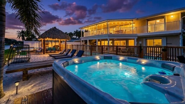 A two-story building with a swimming pool, lounge chairs, and a thatched-roof structure. - Waterfront Villa | BBQ, Pool, Cinema and Tiki (Palm Beach Gardens)