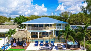 A two-story house with a pool, lounge chairs, and a hot tub. - Waterfront Villa | BBQ, Pool, Cinema and Tiki (Palm Beach Gardens)