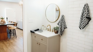 A bathroom with a sink, mirror, towel rack, and a door leading to a dining area. - Hidden Gem Studio Behind Shopaholics Only Boutique (Red Bay)