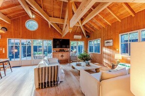 Ein Holzinnenraum mit hohen Decken, großen Fenstern, einem Kamin und einem Fernseher.