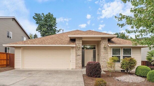 Une maison de plain-pied avec un garage, une porte d’entrée et un petit jardin à l’avant, agrémenté d’aménagements paysagers.
