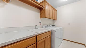 A kitchen with wooden cabinets, a white countertop, a sink, a stove, and a washing machine.