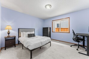A bedroom with a bed, a desk, a chair, a lamp, and a window. - 3 Bedroom House in Suburban Retreat (Gresham)