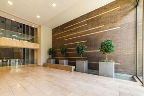 A spacious lobby with a modern design, featuring a brick wall, a glass railing, and potted plants. - Chic 2 Bedroom Apartment for 3 with Pool And Gym (Las Condes)