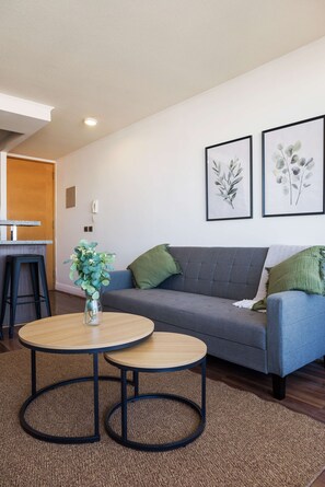 A modern living room with a grey sofa, two round tables, a vase with green foliage, and two framed botanical prints on the wall. - Bright 1BR Las Condes  Apartment in Prime location (Las Condes)